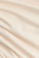 Top de punto de crepé color beige, de ajuste ceñido, con mangas largas y escote redondo. Presenta un diseño con frunces en un hombro y en un lateral que genera un efecto drapeado.