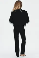 Blazer corto de corte recto con cuello de solapa, manga larga y hombreras. Presenta un diseño minimalista sin botones y forro interior a tono.