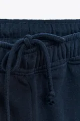 Pantalón de felpa de tiro alto con cintura elástica y corte recto. Cuenta con bolsillos laterales ocultos en la costura y bajo ajustable con cordón elástico y stoppers.