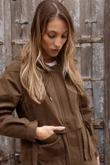 Gabardina liviana color beige con capucha, cierre frontal oculto y cintura ajustable mediante cordón. Presenta bolsillos delanteros amplios y mangas largas con puños rectos.