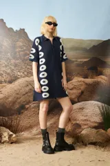 Vestido corto de punto jacquard color azul marino, con diseño de estrellas blancas alineadas verticalmente en los laterales. Presenta cuello polo con cierre frontal de botones y mangas cortas con detalles de rayas en contraste.