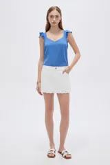 Short pollera de color blanco marfil, tiro alto, con diseño cruzado en el frente y borde inferior con detalles scalloped y perforados.