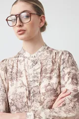 Camisa de manga larga con cuello con bolados y botones nacarados. Presenta un estampado romántico de inspiración barroca en tonos marrón y beige claro.