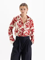 Camisa de poplin de algodón con estampado floral y de fresas en color rojo sobre base crema. Presenta cuello camisero, cierre frontal con botones y mangas largas con puños abotonados.