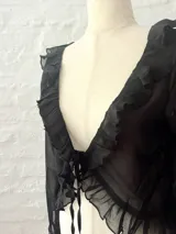 Blusa corta negra de mangas largas acampanadas, con volados en el escote y lazo ajustable en el frente.