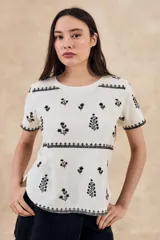 Remera de algodón color blanco con bordados florales y geométricos en color negro. Presenta cuello redondo, mangas cortas y un diseño con franjas horizontales bordadas.