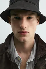 Cazadora de corte relajado confeccionada en piel con acabado de ante. Presenta cuello subido, cierre frontal de cremallera oculta por solapa con botones a presión, bolsillos de plastrón con solapa en el pecho y bolsillos de vivo en la cadera. Incluye trabillas en los hombros, mangas largas con puños abotonados y bajo con elástico.