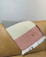 Pashmina de tejido liviano con diseño de bloques de color en tonos crema, naranja y negro, con terminación de flecos blancos en los extremos y etiqueta de cuero decorativa.