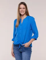 Blusa de calce relajado, color azul vibrante, confeccionada en tela liviana con textura sutil. Presenta escote en V con abotonadura frontal, bolsillo parche en el pecho, mangas largas regulables con presilla y un nudo ajustable en el ruedo frontal.