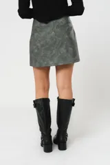 Minifalda gris con textura símil cuero, corte irregular con sobrefalda y cierre frontal con broches metálicos.