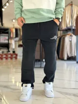 Pantalón de jogging oversize negro con felpa, de corte recto y cordón ajustable en la cintura. Presenta un pequeño estampado de texto blanco en el lateral izquierdo.