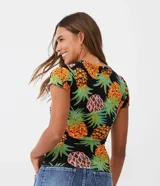 Top de manga corta ajustado al cuerpo, confeccionado en tejido acanalado (ribana) negro con estampado de piñas en tonos naranja, rosa y verde. Presenta detalles de volado (frufru) en los bordes de las mangas y el ruedo inferior.