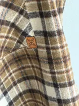 Camisa de viyela con estampado de cuadros en tonos marrones, beige y negro. Presenta cuello clásico, cierre frontal con botones, mangas largas con puños abotonados y dos bolsillos delanteros con solapa.