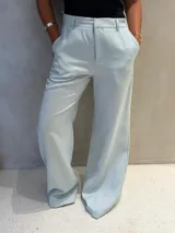 Pantalón de vestir celeste con corte sastrero, tiro alto, pernera recta y ancha, bolsillos laterales y trabillas para cinturón.