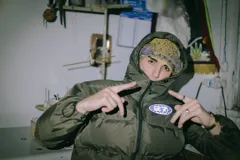 Campera puffer verde oliva con cierre frontal, capucha y logo estampado en el pecho.