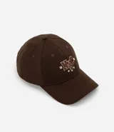 Gorra de sarga de algodón color marrón oscuro con visera curva y ajuste trasero. Presenta un bordado frontal con las letras 'NYC' en estilo universitario con detalles en rojo y blanco, flanqueadas por los números '19' y '86' y tres estrellas blancas debajo.