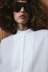 Camisa amplia de algodón con cuello redondo, manga por debajo del codo con puño y bajo asimétrico con aberturas laterales. Presenta cierre frontal con botones ocultos por solapa.