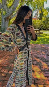 Vestido midi de silueta recta, con escote en V profundo y cuello camisero en contraste. Presenta cierre frontal con botones, mangas largas con leve volumen y tajos laterales. Diseño versátil que puede utilizarse como vestido o como camisero.