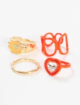 Set de anillos de metal y plástico con talles surtidos. Incluye un anillo dorado con forma de flor y carita sonriente, un anillo dorado liso, un anillo naranja con forma de corazones entrelazados y un anillo naranja con un cristal en forma de corazón.