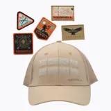 Gorra tipo trucker color beige con paneles frontales de tela y malla trasera. Cuenta con paneles de velcro en la parte frontal para colocar parches intercambiables, visera curva y logo de la marca estampado en el lateral.