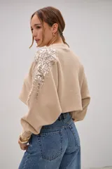 Sweater crop de punto color beige, con cuello redondo, mangas largas abullonadas y puños acanalados. Presenta detalles bordados con lentejuelas y perlas en la zona de los hombros.