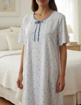 Camisón de algodón blanco con estampado de rayas verticales finas y pequeños puntos azules. Presenta cuello redondo con ribete azul y detalle de moña frontal, con mangas cortas y corte recto hasta la rodilla.