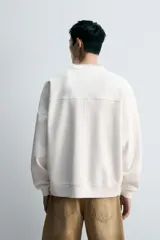 Sudadera negra de corte relaxed fit, confeccionada en tejido técnico interlock de algodón con elasticidad. Presenta cuello redondo, manga larga y una etiqueta aplicada en el bajo. Los acabados son en rib.