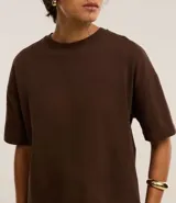 Blusa básica de mujer color negro, confeccionada en malla encorpada de algodón, con cuello redondo y mangas cortas de corte oversized con sisas desplazadas.