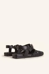 Sandalias planas tipo huarache de cuero negro, con tiras entrelazadas a mano y tira ajustable en el talón con hebilla metálica.