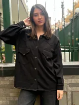 Camisa de estilo western en color negro, confeccionada en tejido de textura sutil. Presenta cuello clásico, cierre frontal con botones, dos bolsillos delanteros con solapa y costuras decorativas en el canesú que definen su diseño característico.