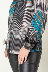 Camisa italiana de satén con estampado abstracto en tonos negro, beige y celeste. Tiene cuello clásico, cierre frontal con botones y mangas largas con puños adornados con plumas negras.