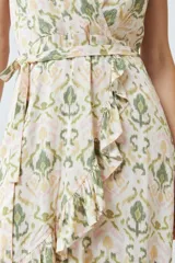 Vestido corto cruzado con estampado abstracto en tonos verde oliva, amarillo y rosa. Tiene escote en V, mangas cortas con volados y falda con volados en el ruedo. Se ata a la cintura con un lazo.