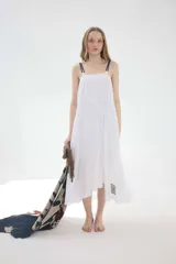 Vestido midi de lino blanco con corte amplio, silueta asimétrica, breteles dobles oscuros y detalles de bordado y costuras irregulares.