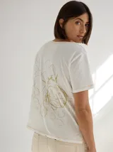 Remera color crudo con estampado en la espalda de una ilustración de una planta con flores.