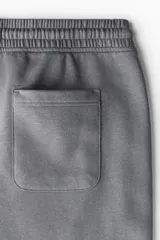 Pantalón deportivo de felpa gris oscuro, con interior cepillado suave. Presenta cintura elástica con cordón de ajuste, bolsillos laterales y puños acanalados en los tobillos. Corte relajado.