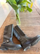 Bota alta plateada de cuero sintético con suela track negra, cierre lateral con cremallera y detalle de hebilla ajustable en el tobillo.