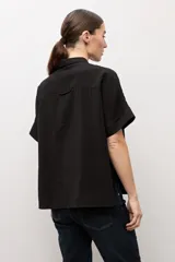 Camisa negra de manga corta, con cuello camisero clásico y cierre frontal de botones.