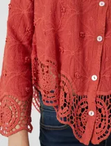 Camisa de algodón con bordado suizo, cuello con solapa y cierre frontal con botones. Presenta mangas largas con terminación de encaje calado y un ruedo asimétrico en pico con un amplio galón de encaje.