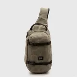 Bolso tipo bandolera de un solo hombro, color verde oliva con acabado texturizado. Cuenta con correas de ajuste frontales con hebillas plásticas negras, cierre lateral y etiqueta de marca en la parte inferior.