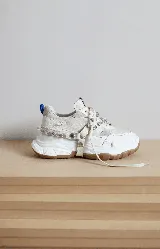 Championes chunky estilo tennis sneakers, color blanco y beige, con detalles en cuero y descarne. Incorporan un arnés desmontable con brillos y tachas, y suela de goma marrón.