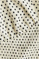Top entallado de punto texturizado blanco con estampado de lunares negros, escote en V pronunciado, mangas cortas con volados y sección inferior fruncida con elástico.