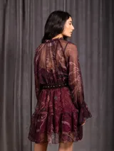 Vestido corto de gasa color marrón con estampado paisley, escote en V con cordones ajustables, mangas largas abullonadas con puños elásticos y falda con volados. Incluye un cinturón negro con hebilla plateada.