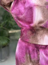 Conjunto de dos piezas compuesto por un buzo corto de manga larga y un pantalón de pierna ancha, confeccionado en tela morley elastizada con estampado tie-dye en tonos fucsia y marrón.