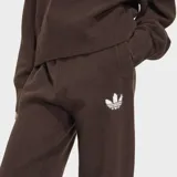 Pantalón de punto Adidas Essentials de color marrón, con diseño holgado y el emblemático logo del Trifolio bordado en blanco en la pierna izquierda.