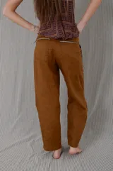 Pantalón sastrero de lino color tostado, con tiro medio, corte flojo que se afina suavemente hacia los tobillos y bolsillos delanteros verticales con vivos decorativos.
