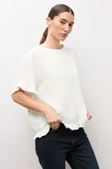 Blusa crudo con textura plumetti, escote redondo y mangas cortas terminadas en delicados volados.