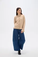 Saco de punto color gris, con cuello redondo, cierre frontal con botones y detalle de volados en la tapeta y el ruedo. Presenta mangas largas con puños acampanados.