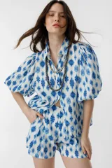 Short de lino blanco con estampado floral azul, de tiro alto, con bolsillos laterales y cierre frontal con gancho metálico.