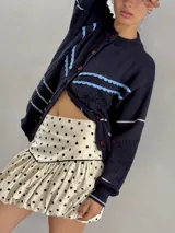 Saco de punto color crema con detalles en crochet verde, cierre frontal con botones y mangas largas.