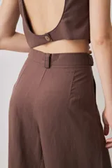 Pantalón de tiro alto color chocolate, con pinzas frontales que aportan caída suave y silueta amplia de pierna recta. Cierra con botón y bragueta, y suma un detalle de botón funcional en la cintura que le da un aire sastrero.